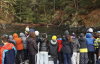 A group of students stand on deck and look out into a secluded bay